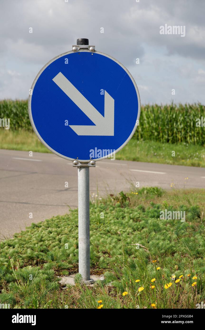A blue and white road sign with an arrow pointing left, indicating a