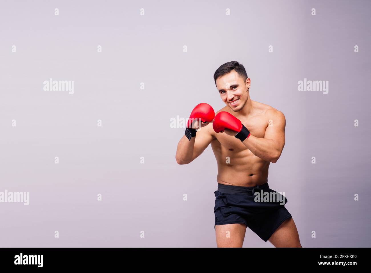 Muscular model sports young man in a boxing gloves on grey background