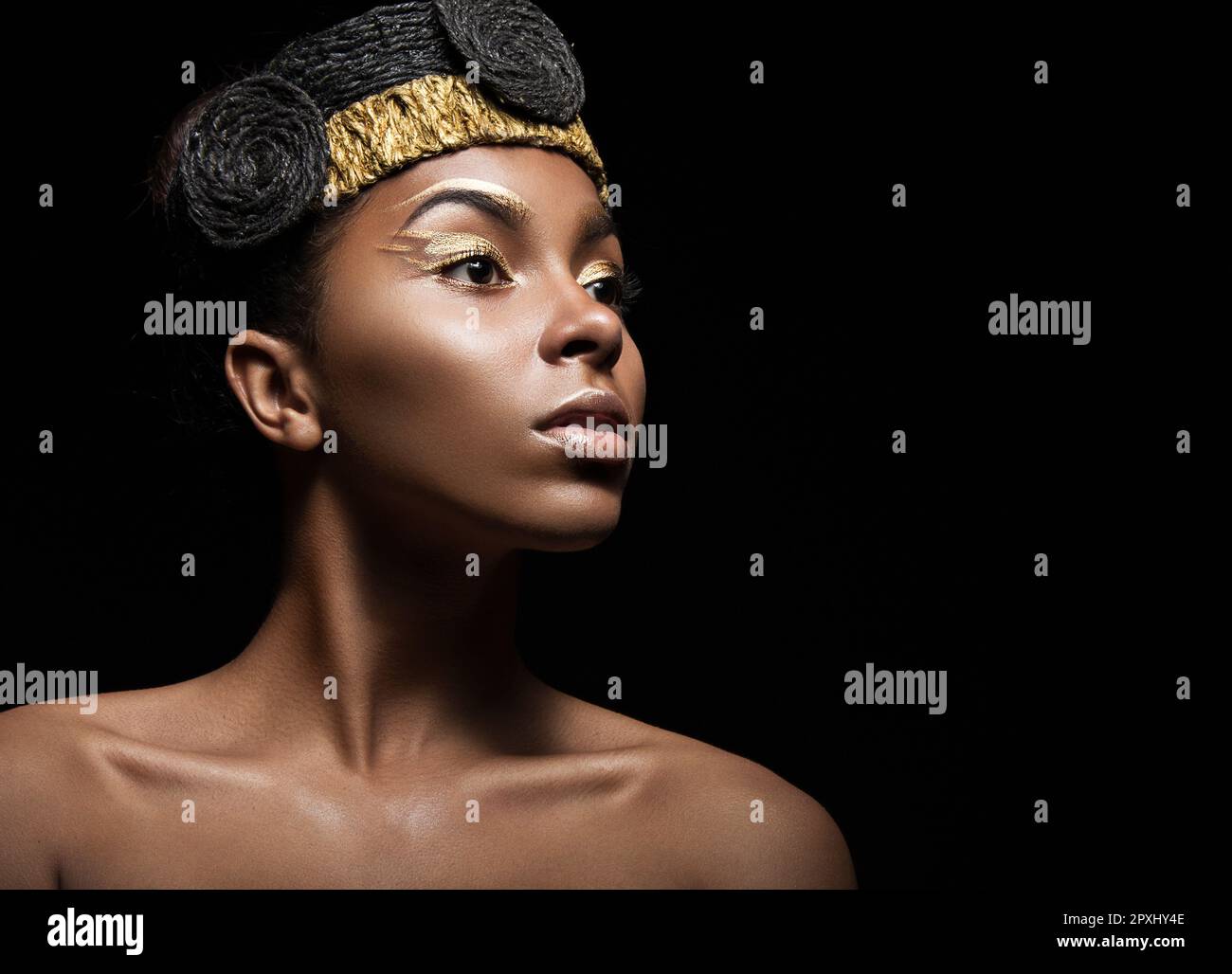 African girl with bright makeup and creative gold accessories on the head. Beauty face. Picture taken in the studio on a black background. Stock Photo