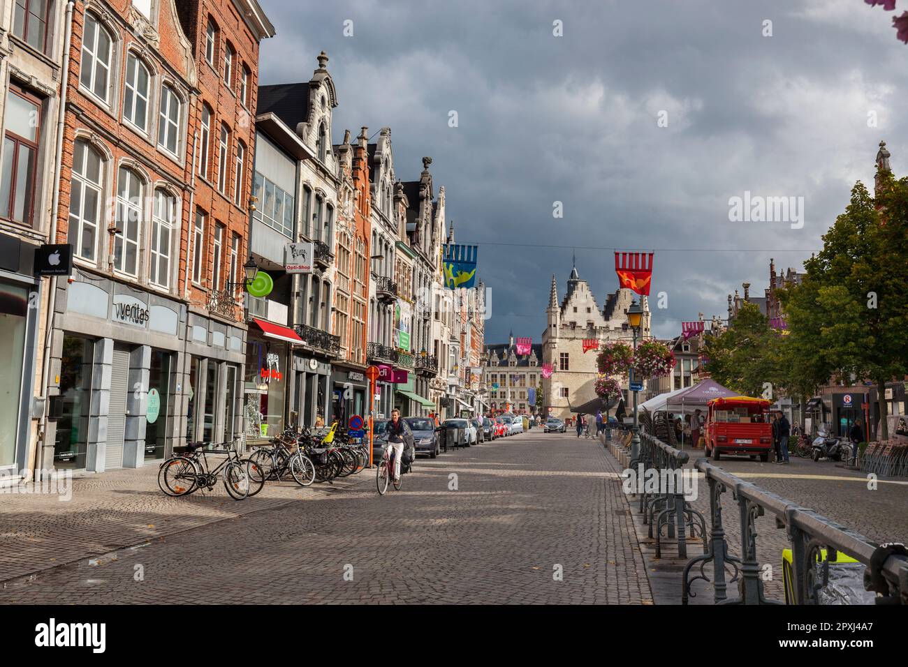 Woman on bicycle in Ijzerenleen with historic gabled shops, cafes and market with Schepenhuis - original town hall in background, Mechelen, Belgium Stock Photo