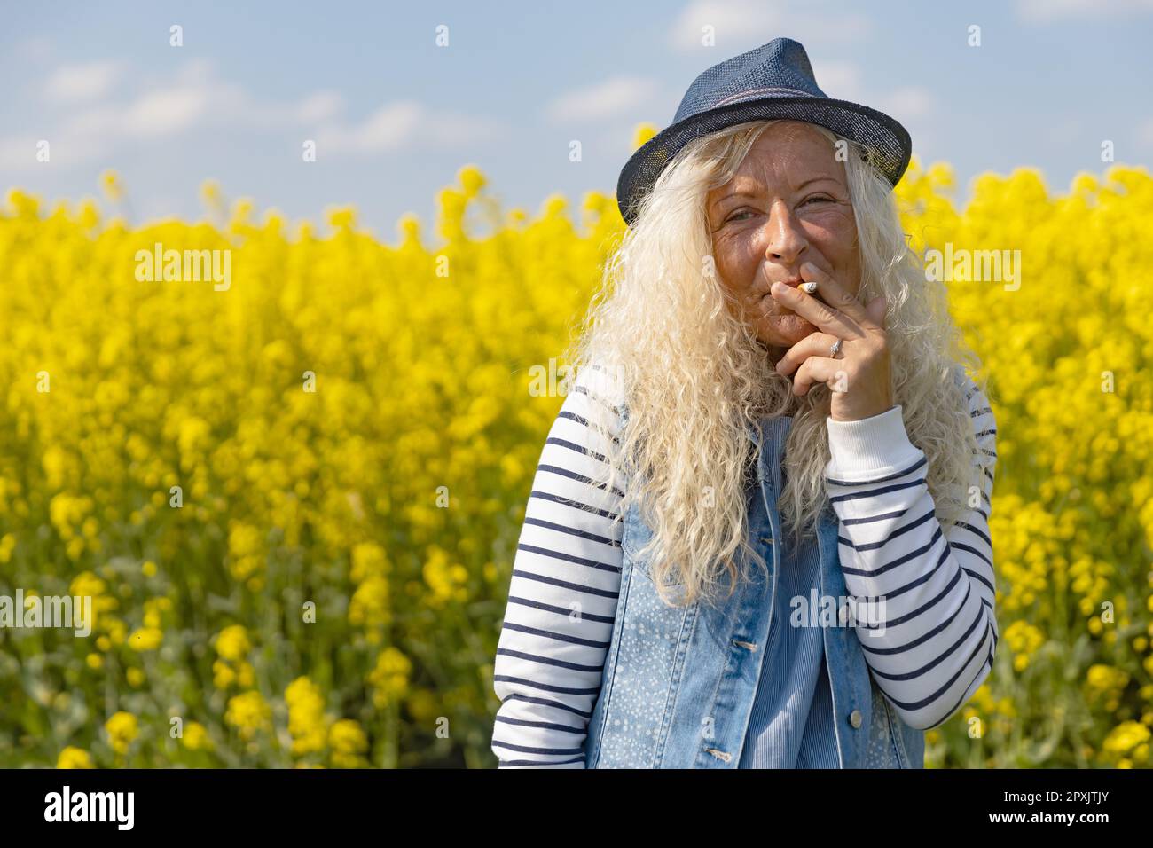 Elderly Woman smoke a cigarette in rape field with yellow blossums Stock Photo