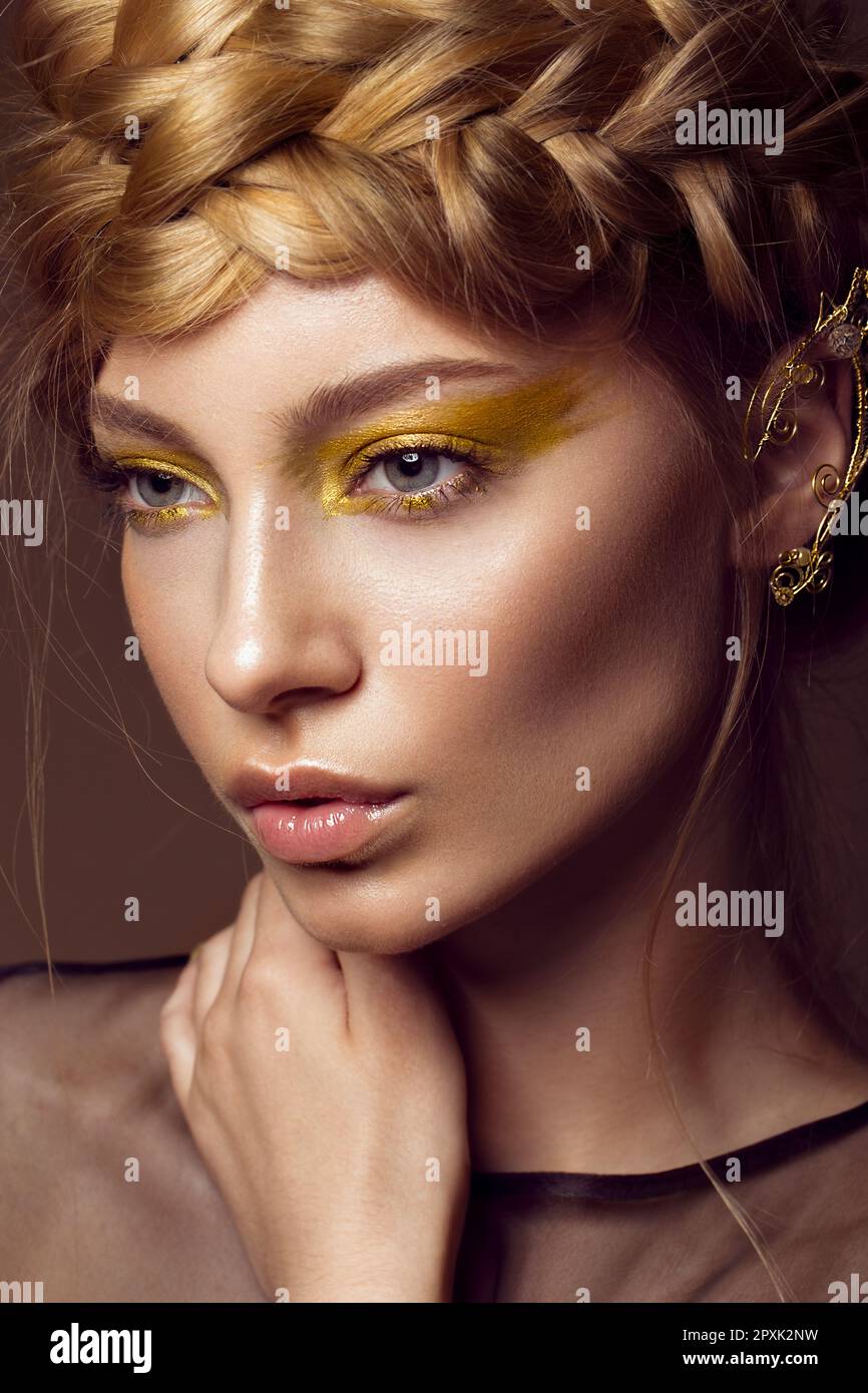 Beautiful girl in a gold dress with creative makeup and braids on her