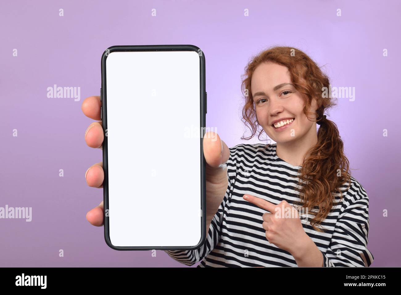 Positive millennial ladie holding smartphone with white blank screen posing on colorful studio background Stock Photo