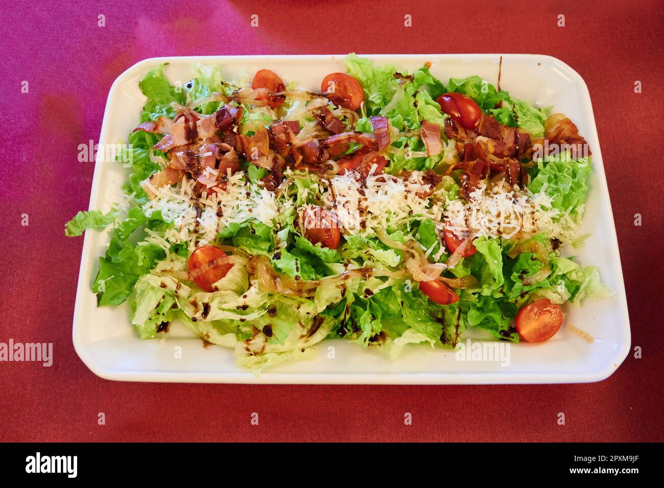 Salad with cheese, bacon, caramelized onion, tomato and lettuce dressed with Modena vinegar Stock Photo