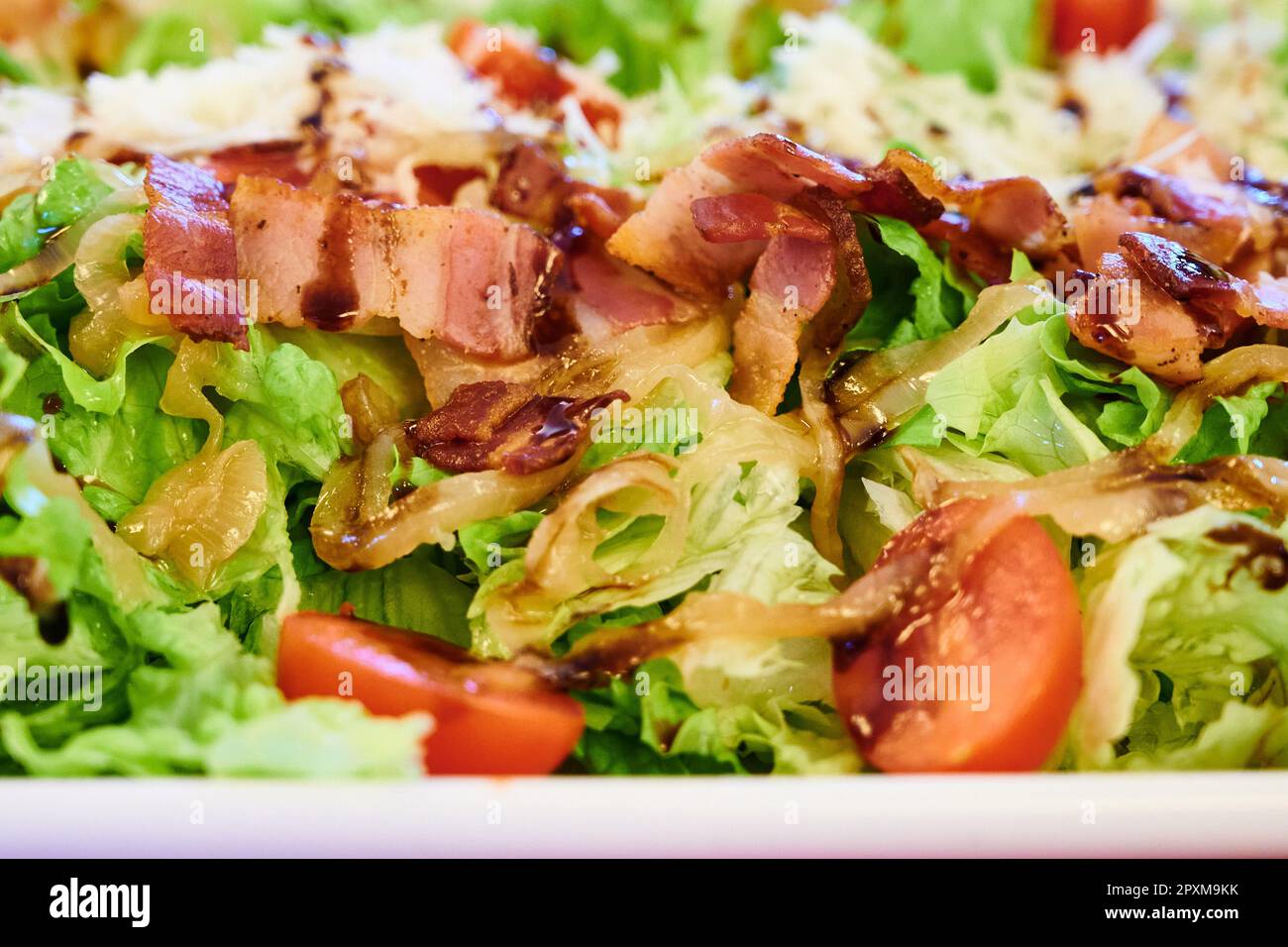 Salad with cheese, bacon, caramelized onion, tomato and lettuce dressed with Modena vinegar Stock Photo
