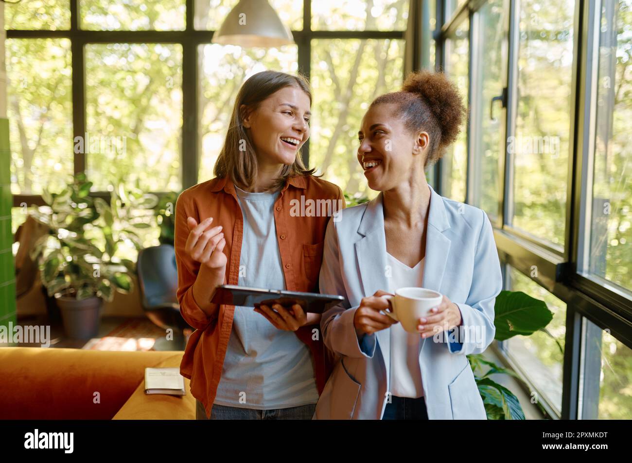 Happy cheerful coworkers chatting and laughing at workplace. Two female employees enjoying teamwork in modern coworking space Stock Photo