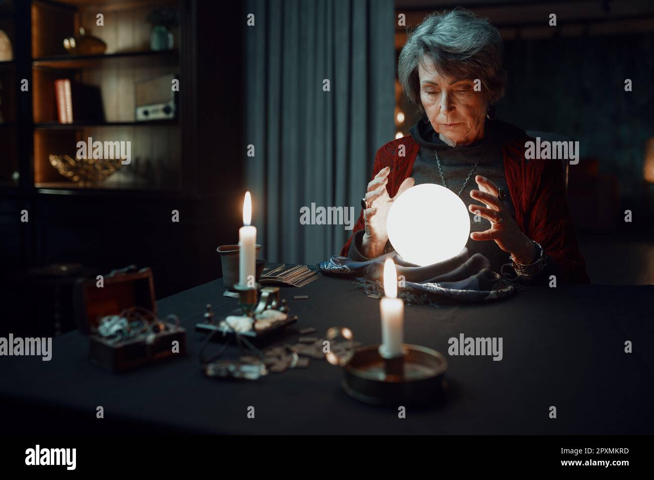 Confident witch fortune teller doing predictions with illuminated crystal ball reading future during esoteric ritual and divination seance Stock Photo