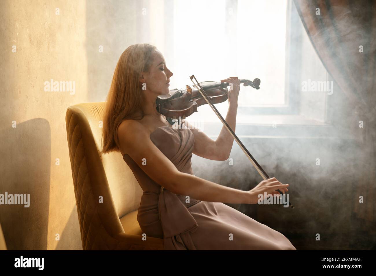 Dreamy elegant woman playing violin sitting on chair in room surrounded
