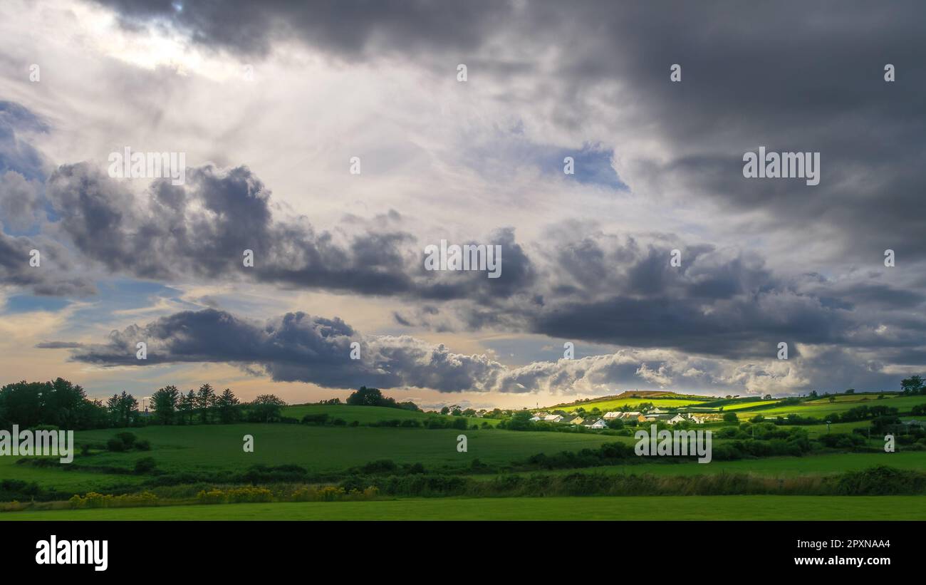 Sky with cumulus clouds over a Irish village on evening. Irish settlement in County Cork, dramatic landscape. European countryside, rustic landscape. Stock Photo