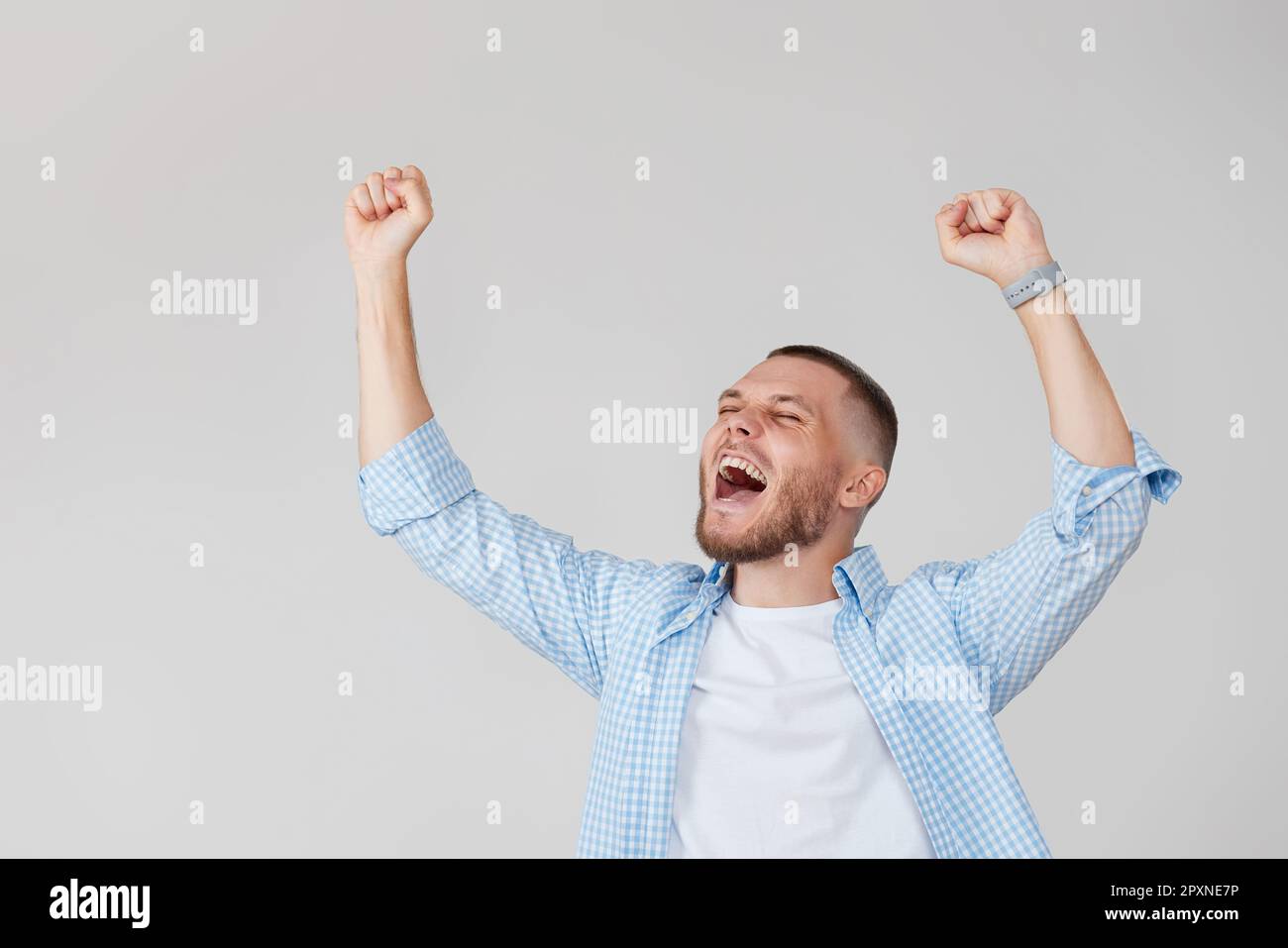 amazed young man celebrating victory on gray background. Stock Photo