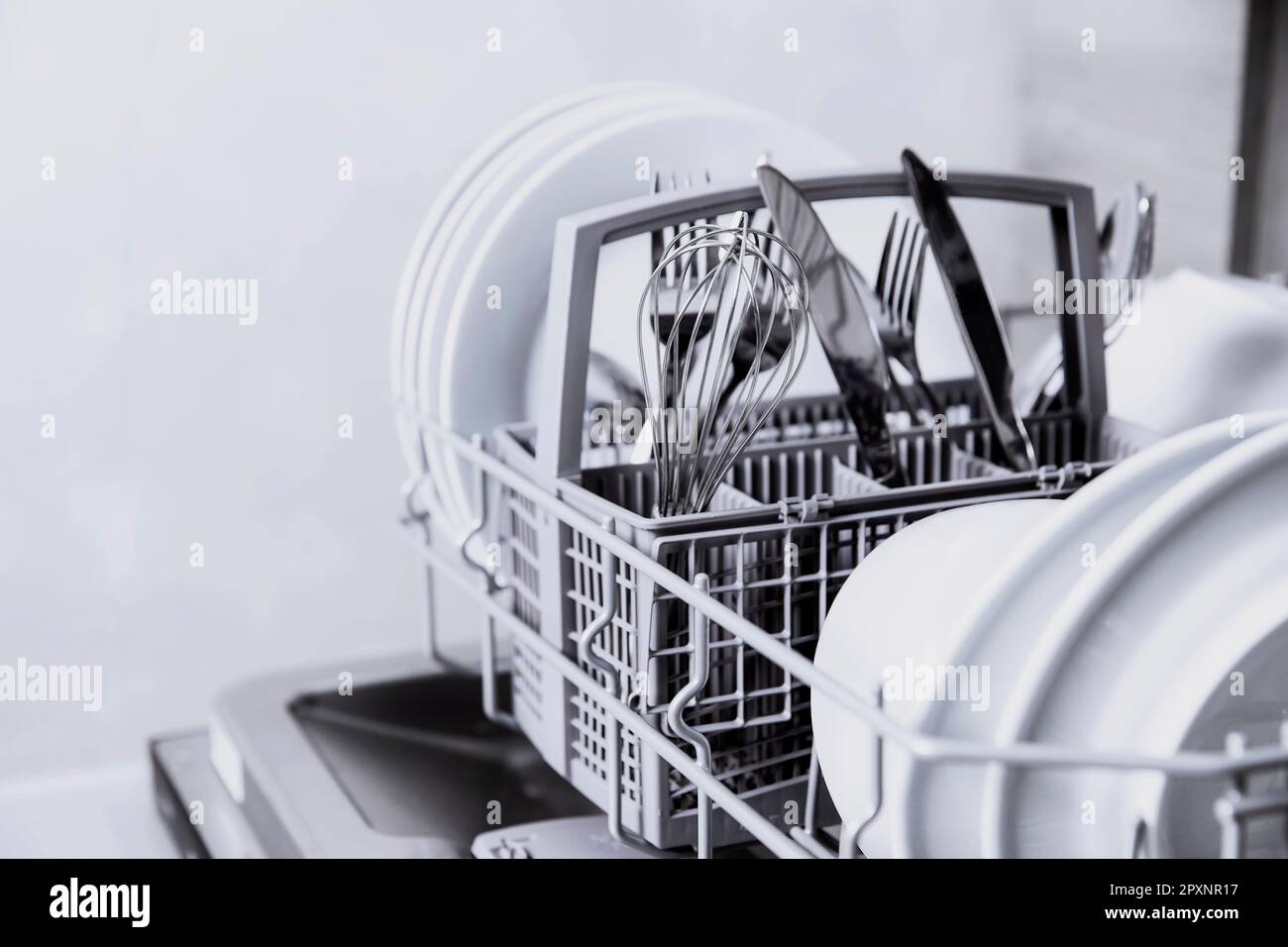 Front view of open automatic stainless steel built-in fully integrated top control dishwasher range machine with clean utensils, cutlery, glasses, dis Stock Photo