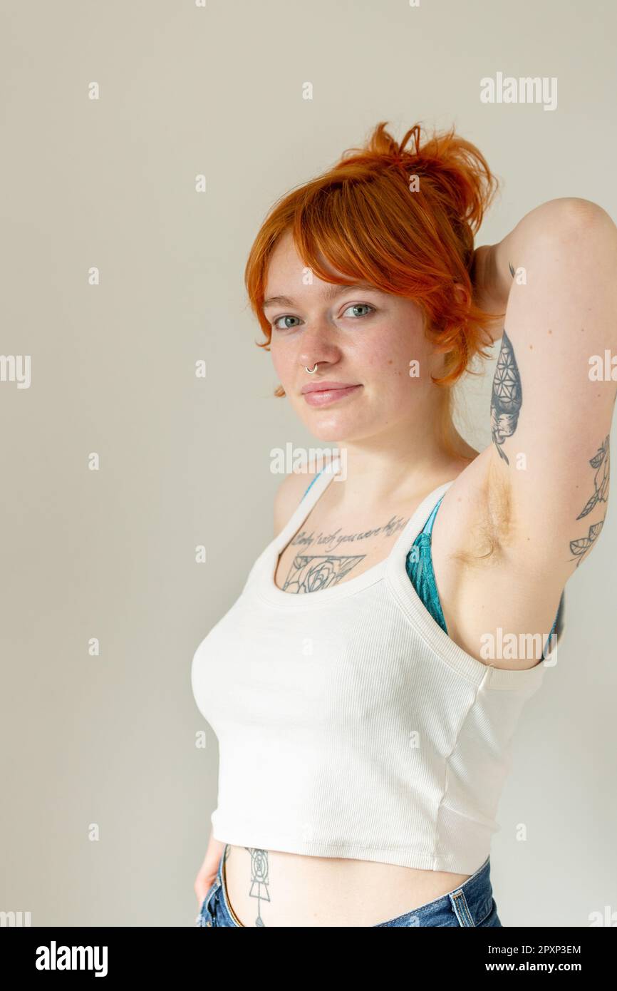 Unshaven young woman smiling cheerfully while wearing a bra and jeans.  Happy young woman embracing her natural body and underarm hair. Body  positive young woman making her own choice about her body.