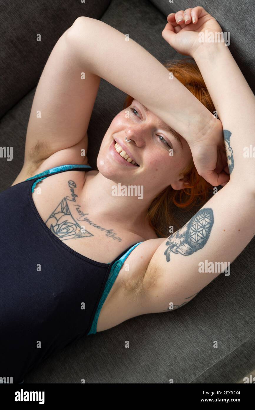 A woman with hairy armpits lying on a sofa with her arms above her head. Stock Photo