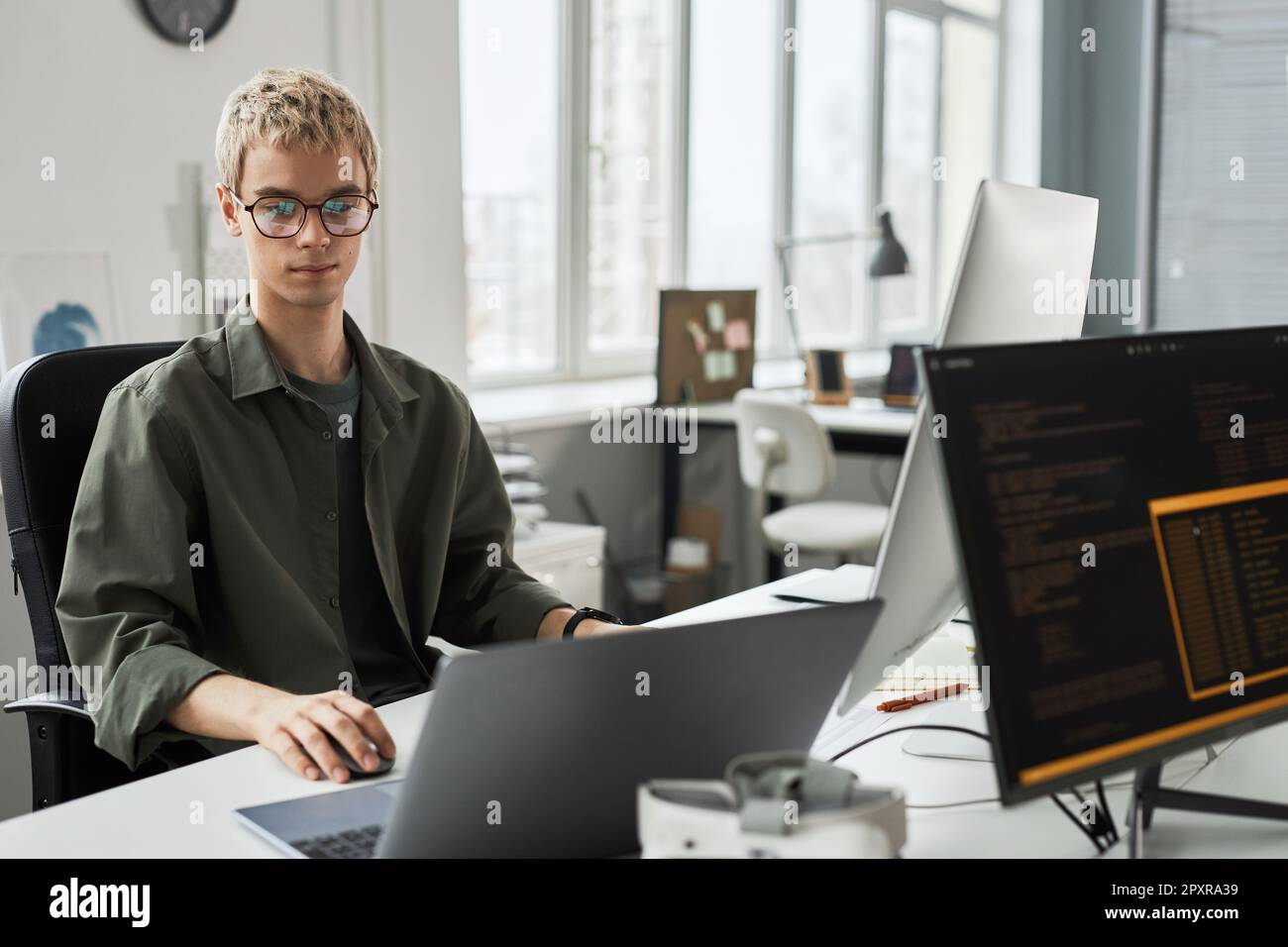 Young programmer in eyeglasses concentrating on his work with codes for new software while sitting at his workplace in office Stock Photo