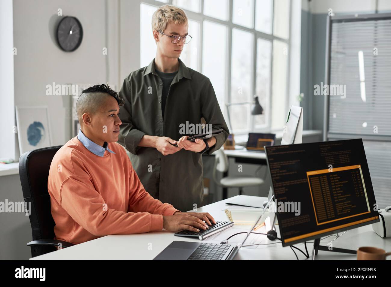 Colleagues working over computer program in team, they sitting at table and typing computer codes on computer Stock Photo