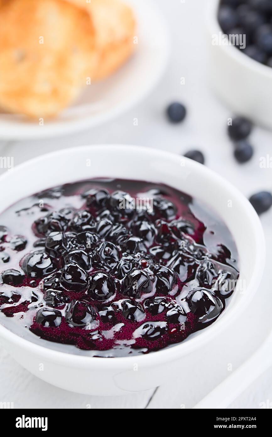 Fresh homemade jam made of Patagonian Calafate berries (lat. Berberis heterophylla), served in white bowl, toasted bread and raw berries in the back ( Stock Photo