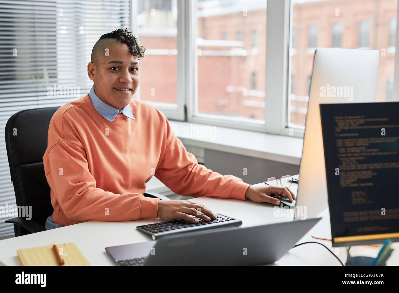 Portrait of young programmer smiling at camera while working with security codes on computer sitting at his workplace Stock Photo