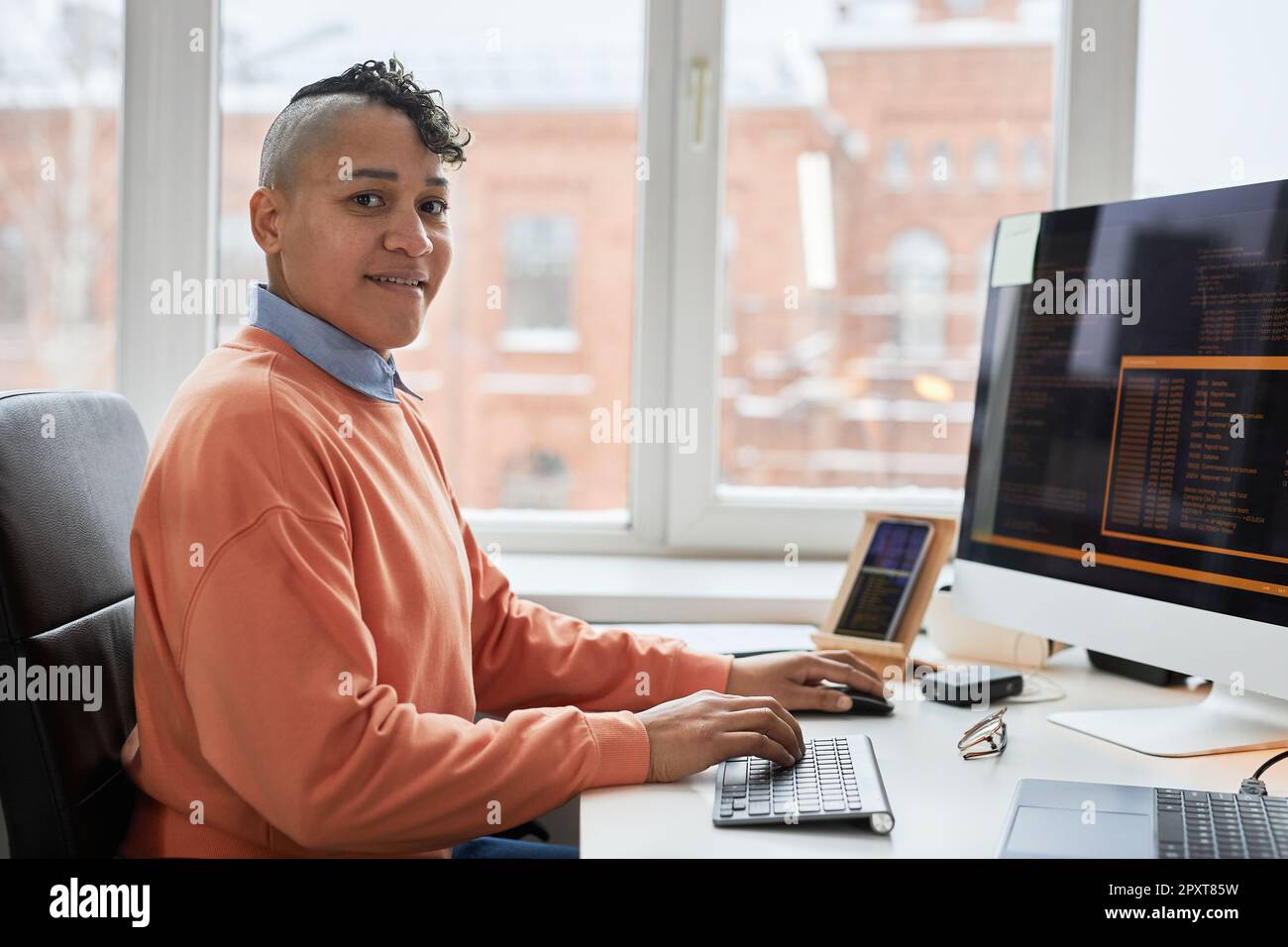 Portrait of professional programmer smiling at camera while writing codes on computer sitting at his workplace Stock Photo