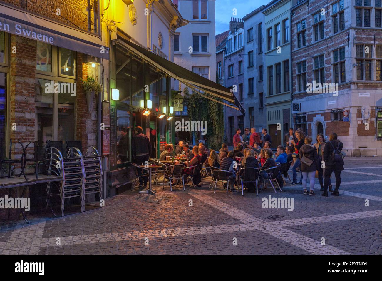 People relaxing and socialising outside cafe, bar restaurant at intersection of Wijngaardbrug and Grote Goddaard Old Town Antwerp at twilight or night Stock Photo