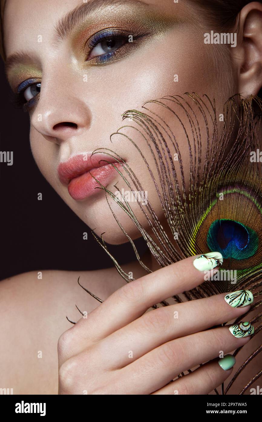 Beautiful girl with bright makeup, manicure design and peacock feather