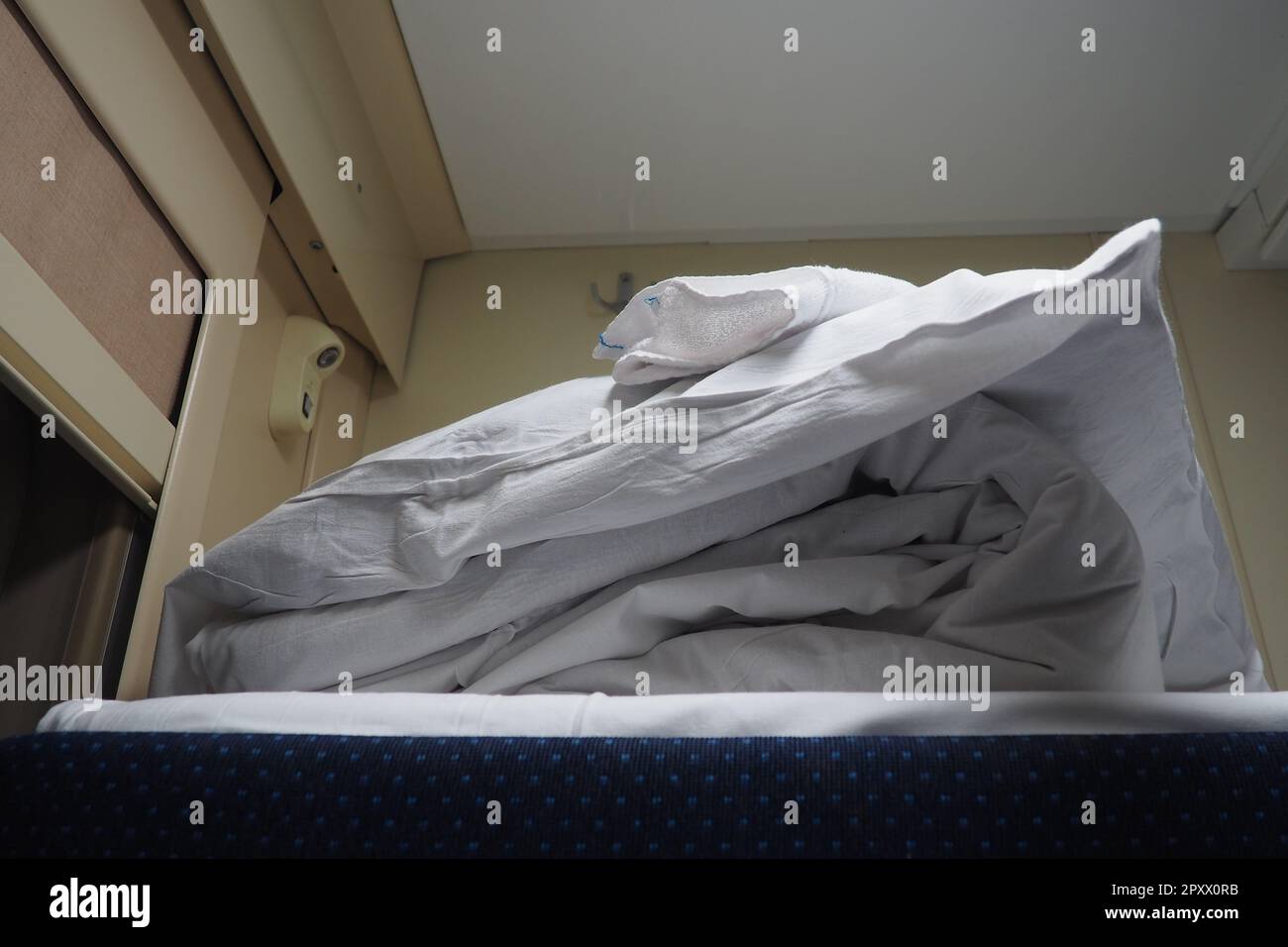 A set of bed linen on the top shelf of a railway car compartment. A bed