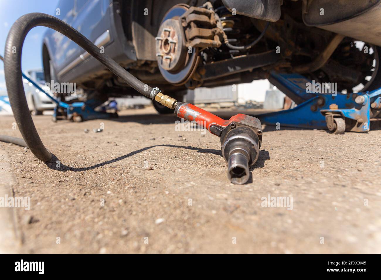Pneumatic wrench tool on the asphalt and a car jack for lift up the body and changing the tire. Car without wheelTire service. Seasonal change or repa Stock Photo