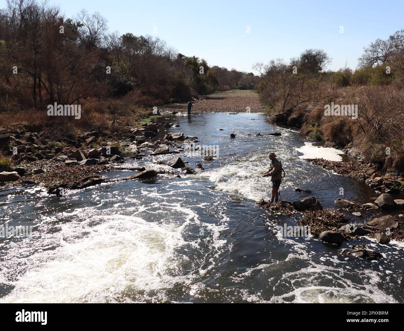 Picture of 2 men fishing in a raging portion of the crocodile river in South Africa , taken in winter when the ground and plants are drier and brown Stock Photo