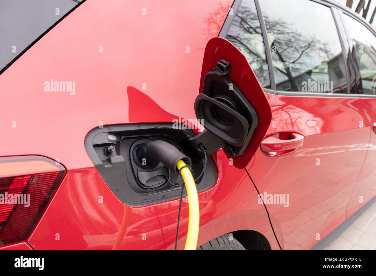 A red car with a black roof and a yellow electric cable stuck in it