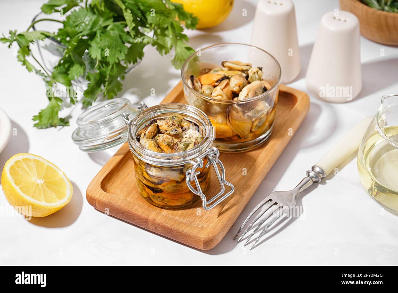 Board with jar and glass bowl of pickled mussels on white background
