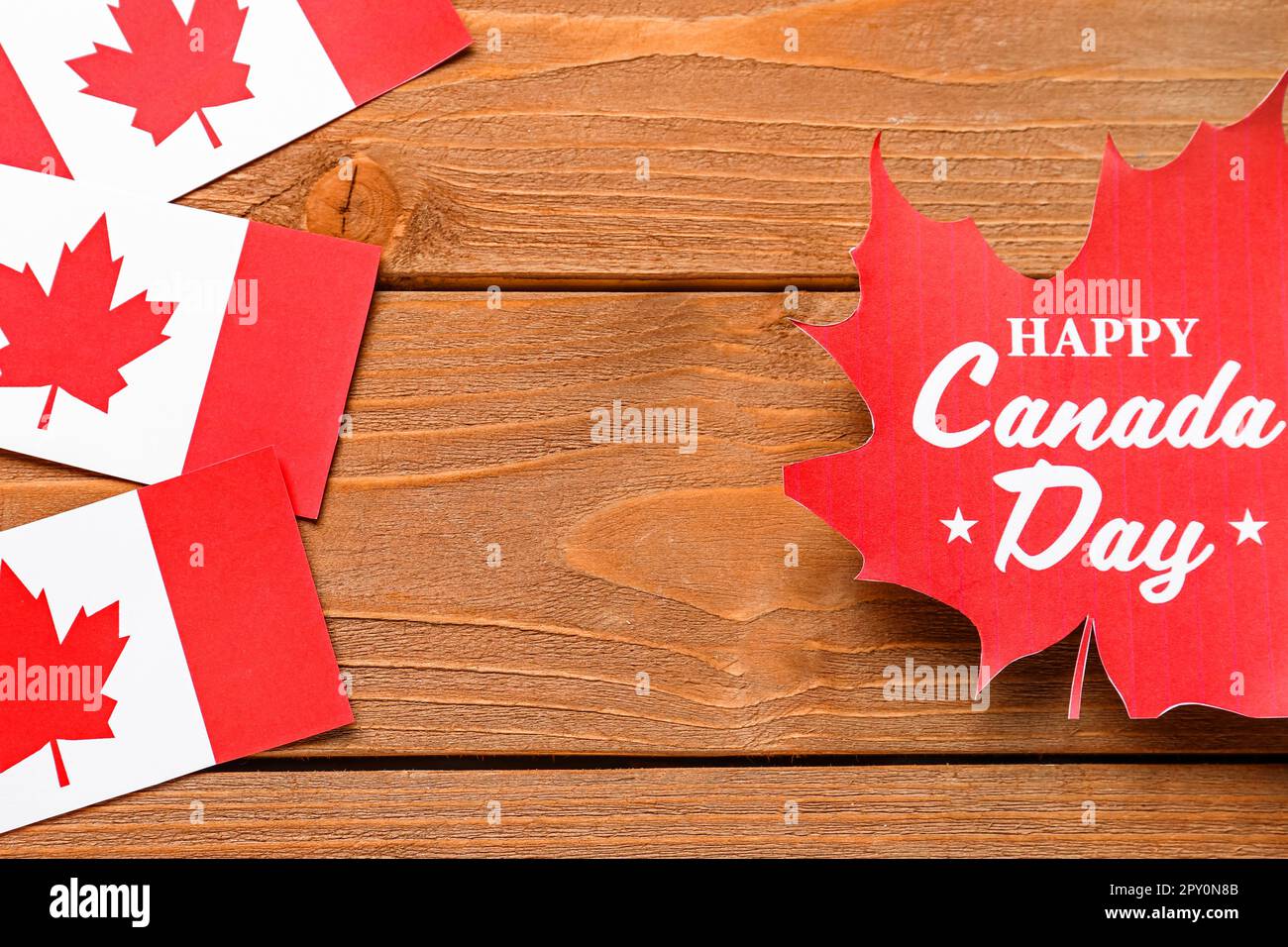Frame made of maple leaf with text HAPPY CANADA DAY and flags on wooden ...