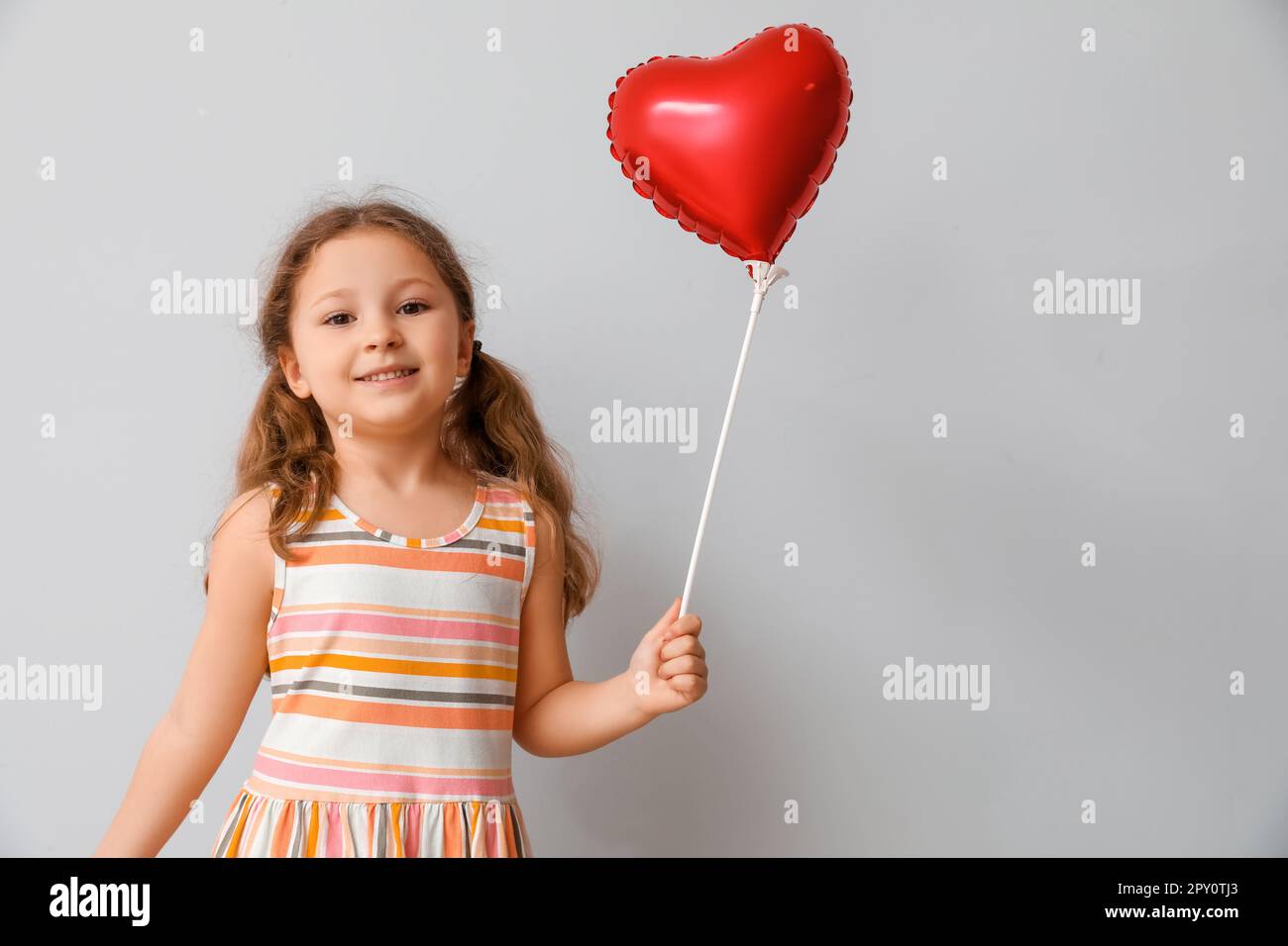 Little girl with heart shaped balloon on light background. Children's