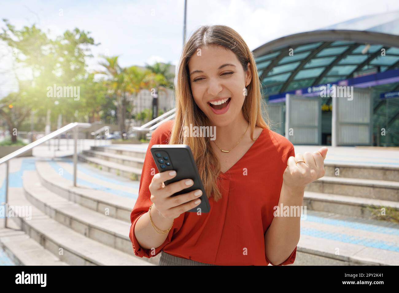 Excited casual woman celebrating good news on her smartphone in Brooklin district of Sao Paulo, Brazil Stock Photo