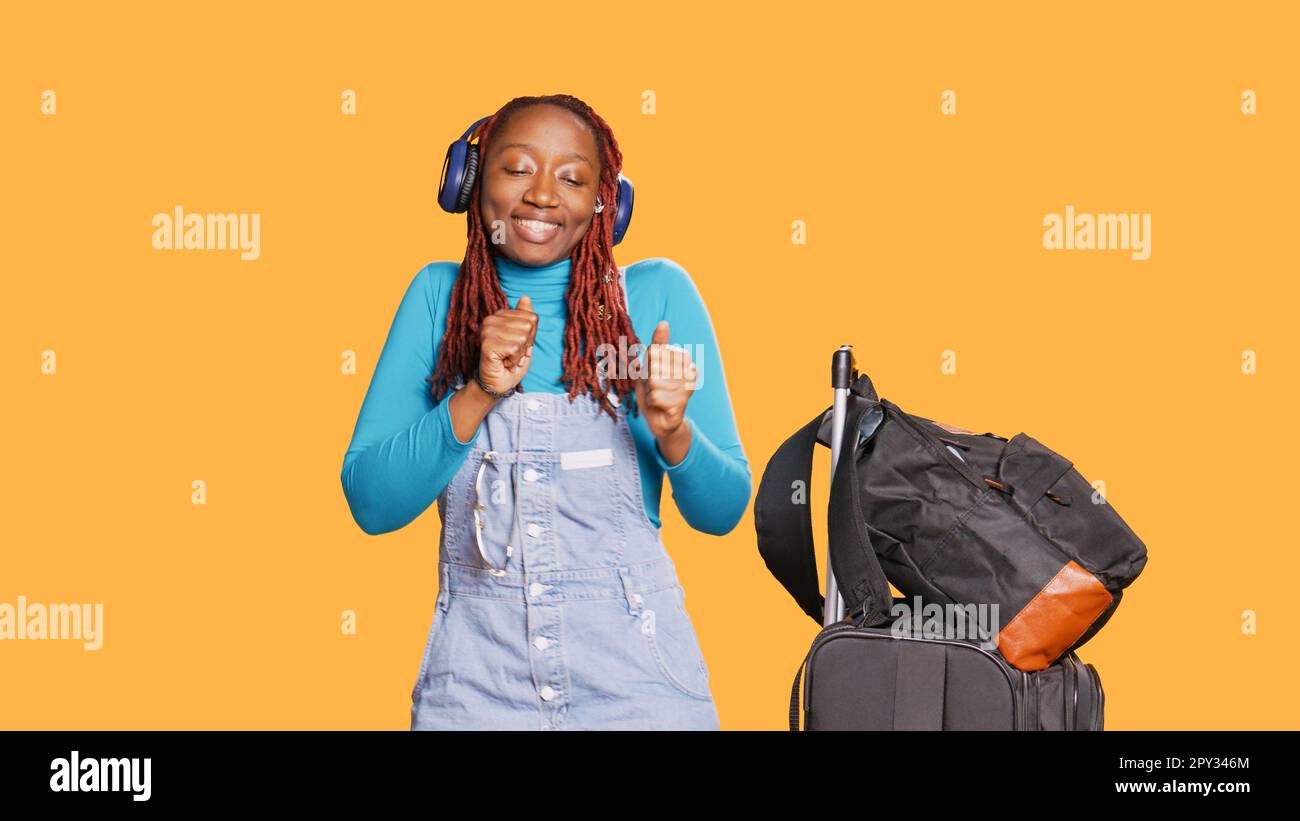 Joyful modern woman dancing on music, using headphones to listen to songs  on camera. Young adult doing dance moves and having fun, enjoying mp3  sounds on vacation trip. Handheld shot Stock Photo -