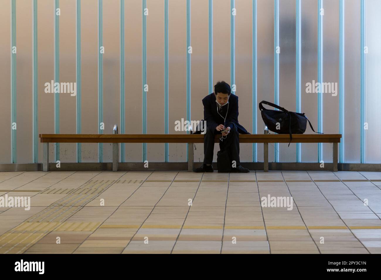 A Japanese male office worker or salaryman sits on a bench to use his ...
