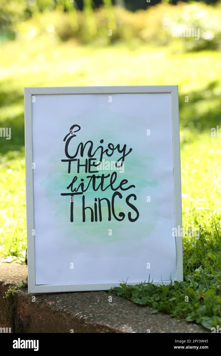 Poster with phrase Enjoy The Little Things on grass outdoors Stock Photo