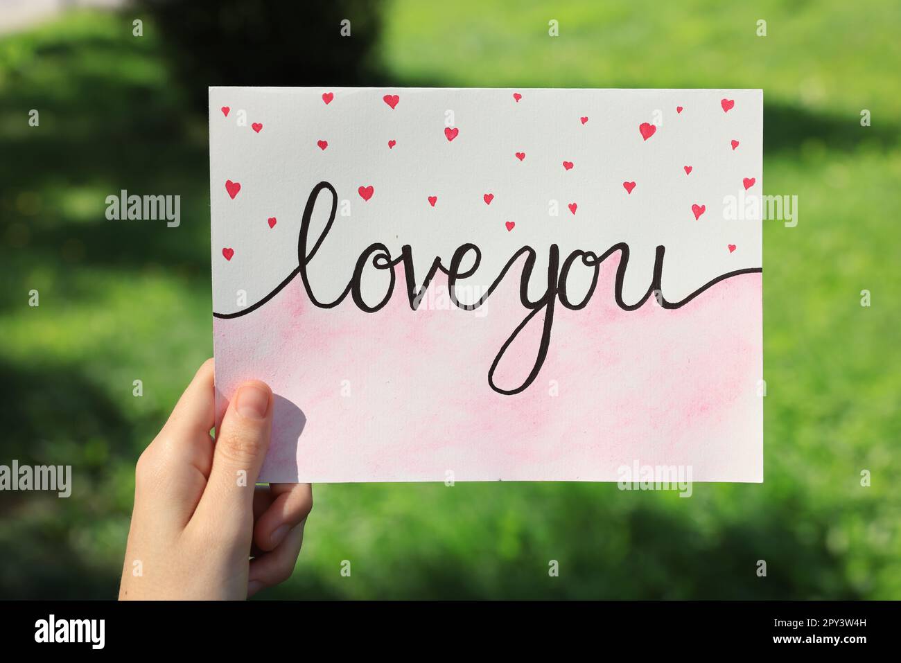 Woman holding card with phrase Love You outdoors, closeup Stock Photo