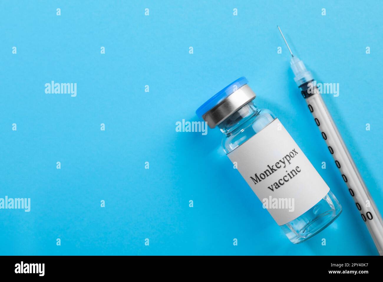 Monkeypox vaccine in glass vial and syringe on light blue background ...