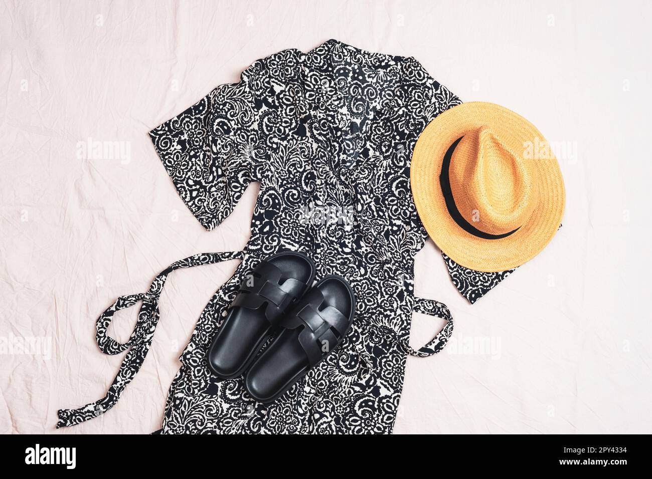 Feminine clothes and accessories with black dress, straw hat and sandals on white background. Overhead view of woman's casual day outfit. Trendy styli Stock Photo
