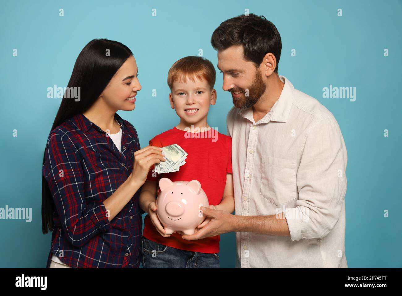 Happy family putting money into piggy bank on light blue background ...