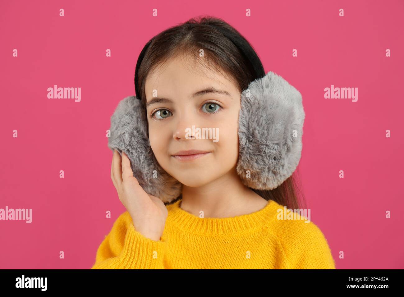 Cute little girl wearing stylish earmuffs on pink background Stock