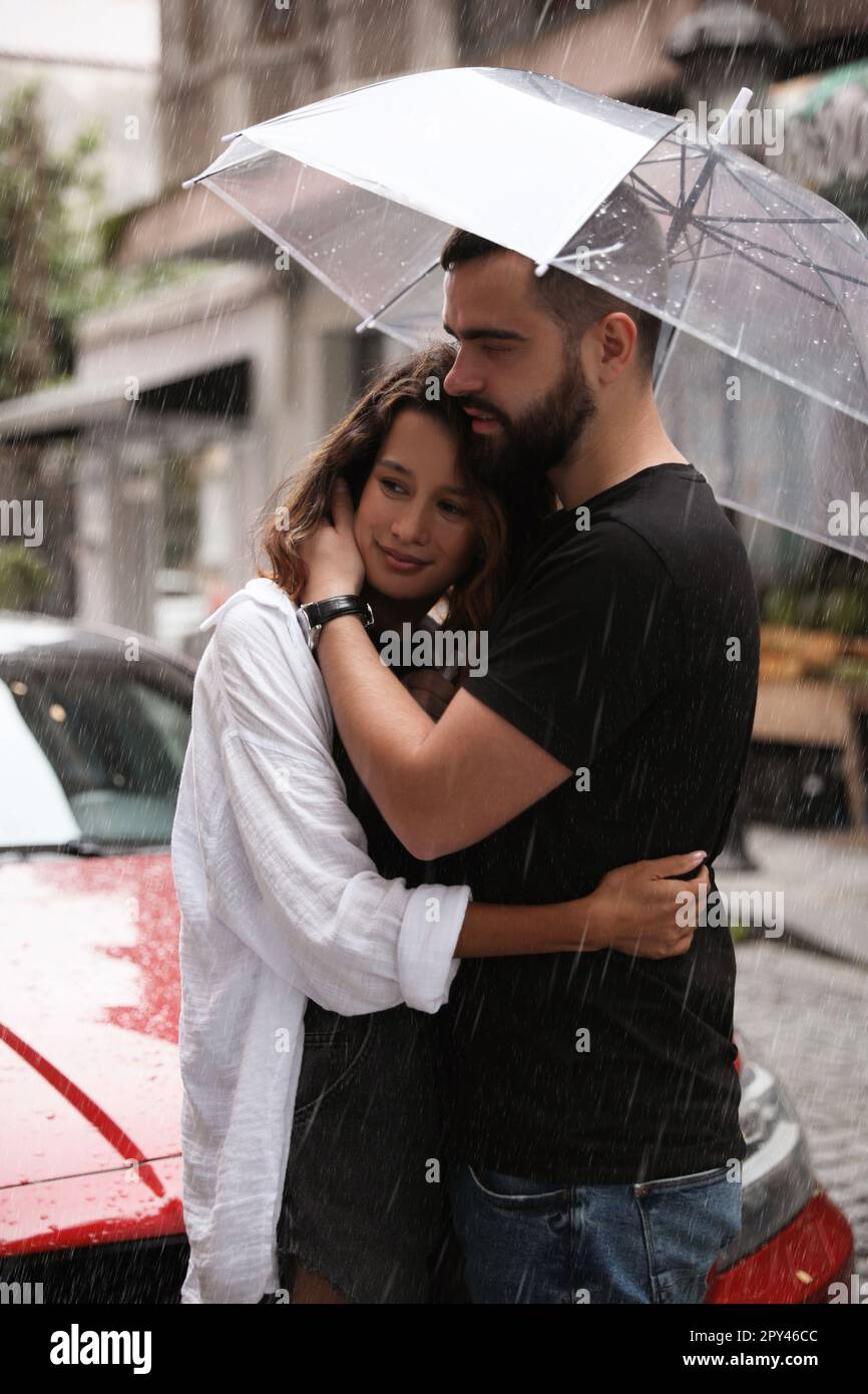 Young couple with umbrella enjoying time together under rain on city street  Stock Photo - Alamy