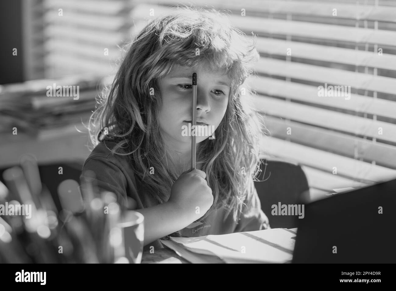 Tired serious schoolboy while doing homework. Portrait school kid siting on table doing homework. Funny child girl doing homework writing and reading Stock Photo