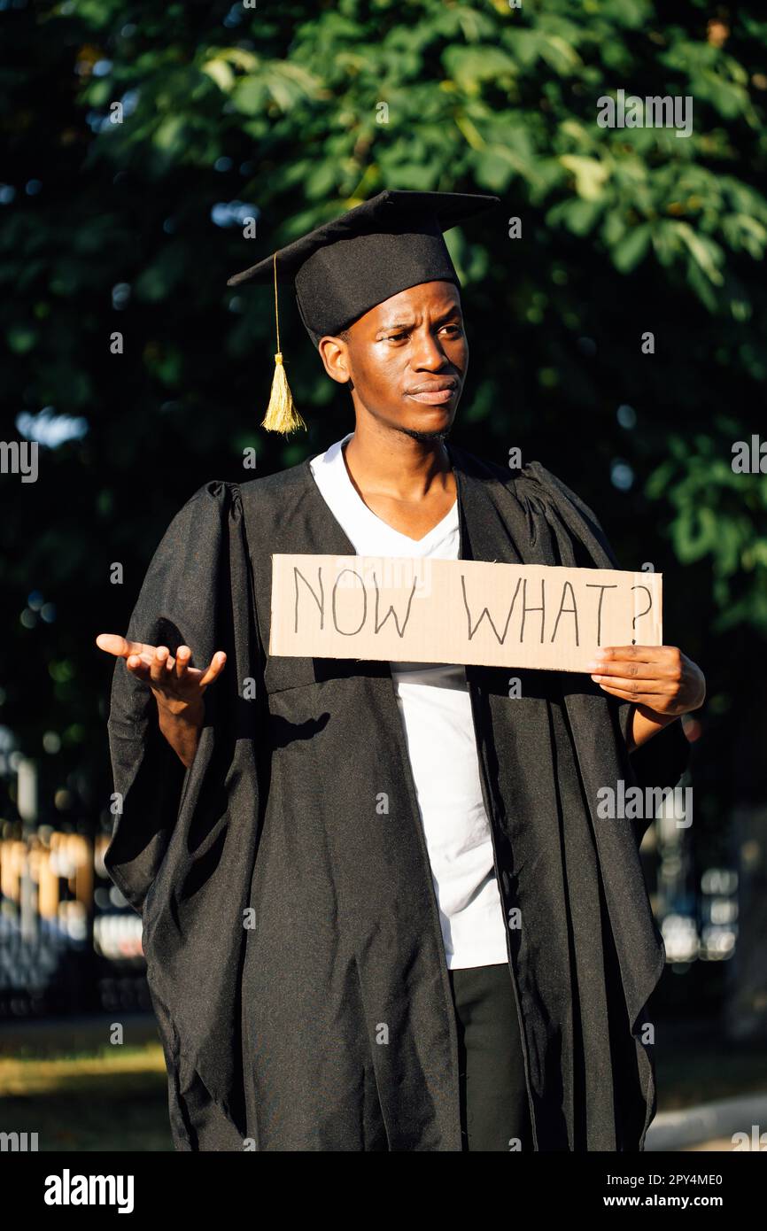 Portrait of disappointed afro american guy holding cardboard poster and lending hand on street. Looking for job, hiring and employment issue Stock Photo