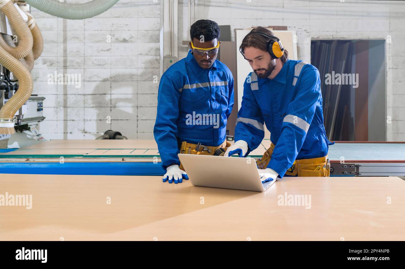 Young caucasian labour in blue mechanic jumpsuit looking at laptop ...