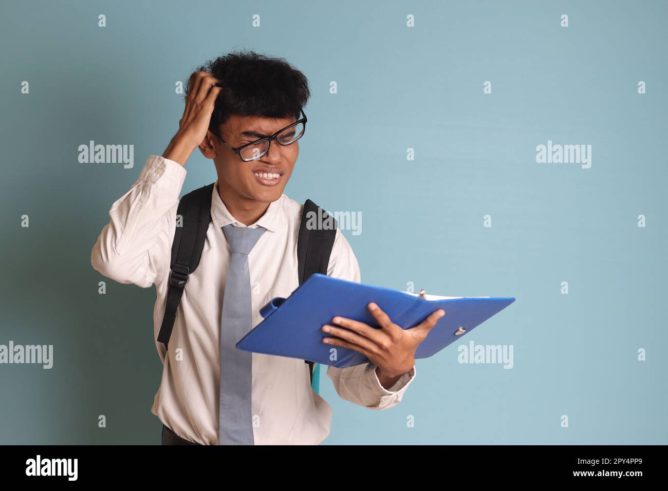 Indonesian senior high school student wearing white shirt uniform with gray tie writing on note book using pen and thinking about an idea. Isolated im Stock Photo