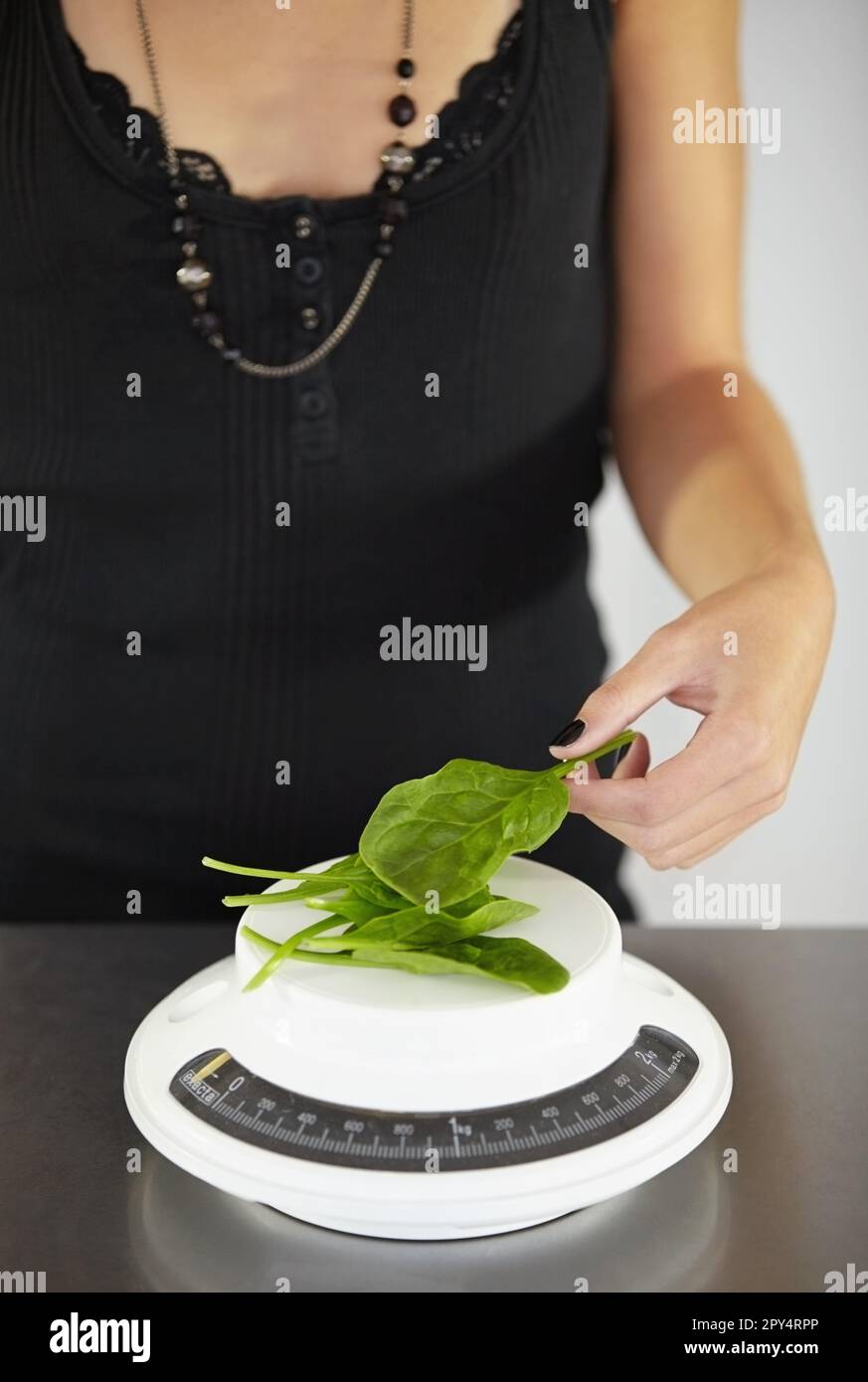 Hand, scale and spinach in kitchen for diet, food or eating disorder