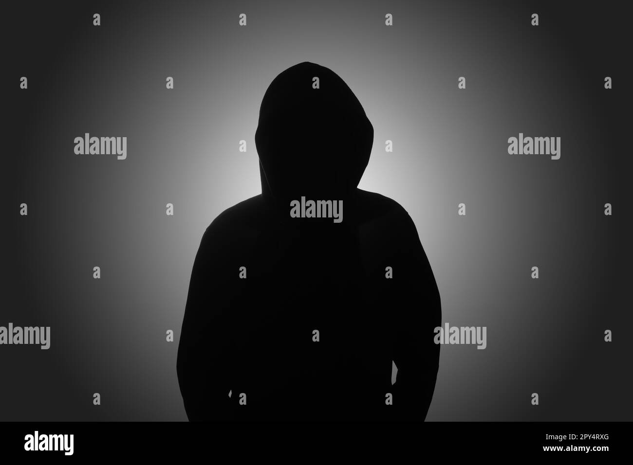 Mysterious man wearing black hoodie standing against dark background. Hacker, crime, and cyber security concept. Stock Photo