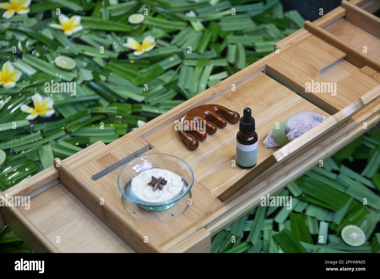 Tub full of water and herbs with wooden bathtub tray with various