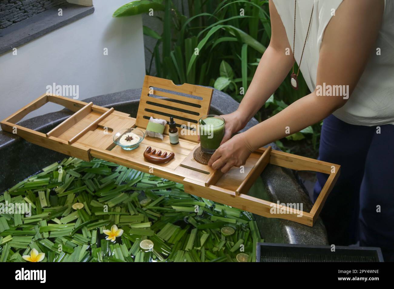 Tub full of water and herbs with wooden bathtub tray with various