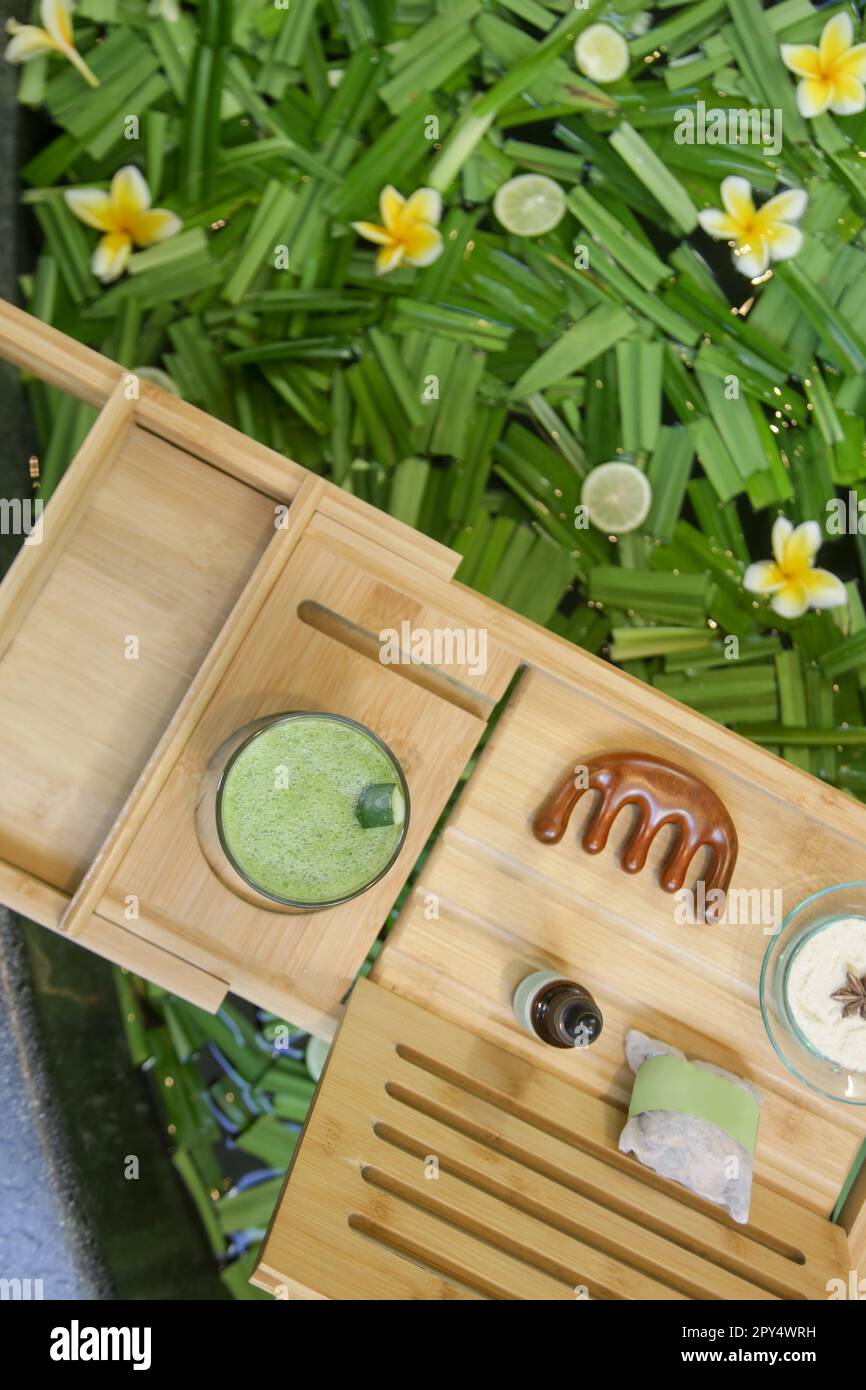Tub full of water and herbs with wooden bathtub tray with various